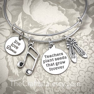 May include: Silver charm bracelet with charms that say "live love dance", "Teachers plant seeds that grow forever", and a music note. The bracelet also has a charm of a pair of ballet shoes.