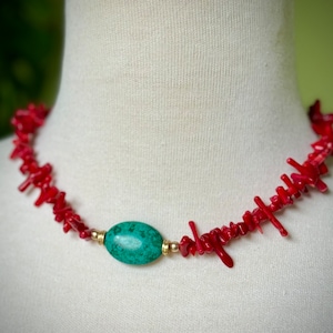 May include: A red coral necklace with a turquoise stone pendant. The necklace is made of small, irregular pieces of coral that are strung together on a gold chain.