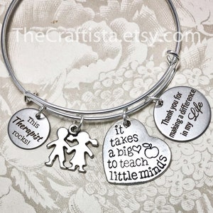 May include: Silver charm bracelet with four charms. The charms say "This Therapist rocks!" "It takes a big heart to teach little minds." "Thank you for making a difference in my life." and features two children holding hands.