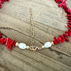 May include: A red coral and pearl necklace with a gold chain and clasp. The necklace is made of small, irregular pieces of coral and white pearls.