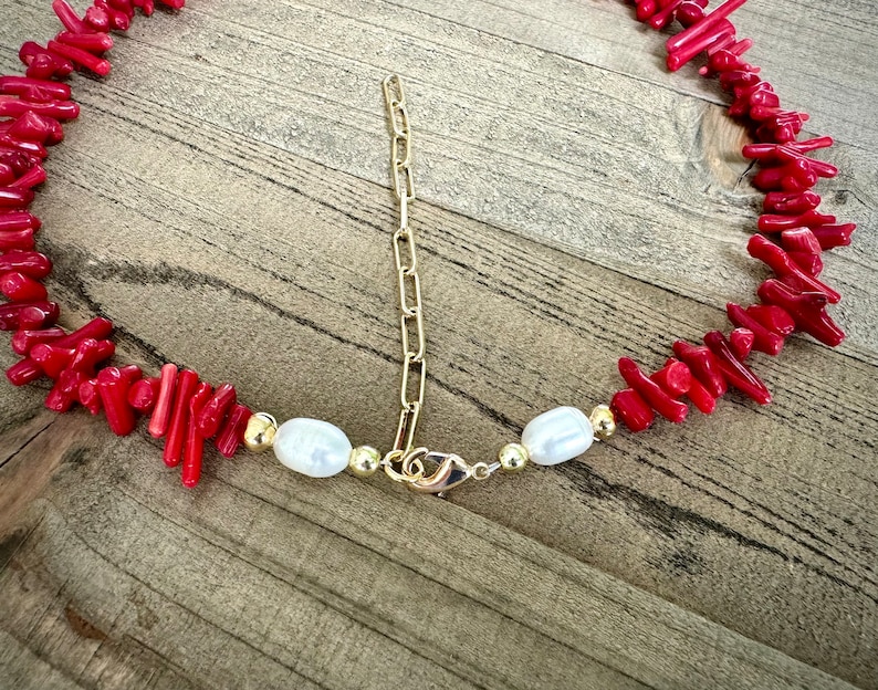 May include: A red coral and pearl necklace with a gold chain and clasp. The necklace is made of small, irregular pieces of coral and white pearls.