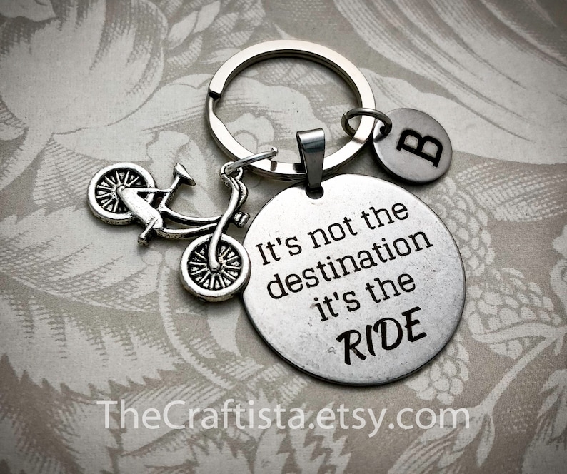May include: Silver keychain with a bicycle charm and a round tag that says "It's not the destination it's the RIDE". The keychain also has a small round tag with the letter "B" on it.