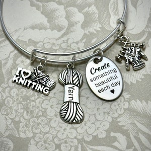 Könnte beinhalten: Silbernes Armband mit Strick-Anhängern, darunter eine Wollknäuel, Stricknadeln und ein Anhänger mit der Aufschrift "Ich liebe Stricken". Das Armband hat auch einen Anhänger mit dem Text "Erschaffe jeden Tag etwas Schönes".