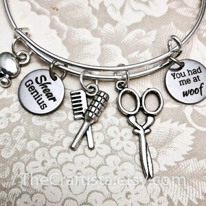 May include: Silver charm bracelet with charms that say "Shear Genius" and "You had me at woof". The bracelet also has charms of a paw print, scissors, a comb, and a brush.