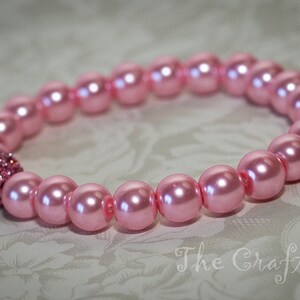 K&ouml;nnte beinhalten: Ein rosa Perlenarmband mit einem glitzernden rosa Strassstein als Mittelst&uuml;ck.