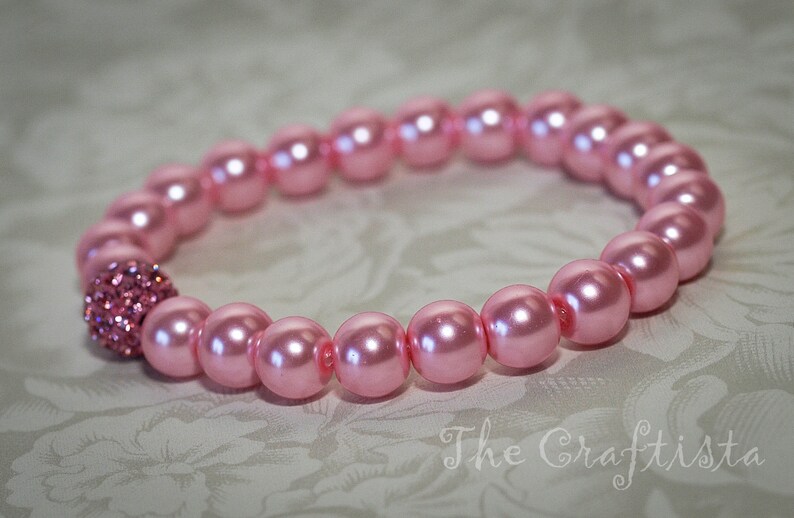 K&ouml;nnte beinhalten: Ein rosa Perlenarmband mit einem glitzernden rosa Strassstein als Mittelst&uuml;ck.
