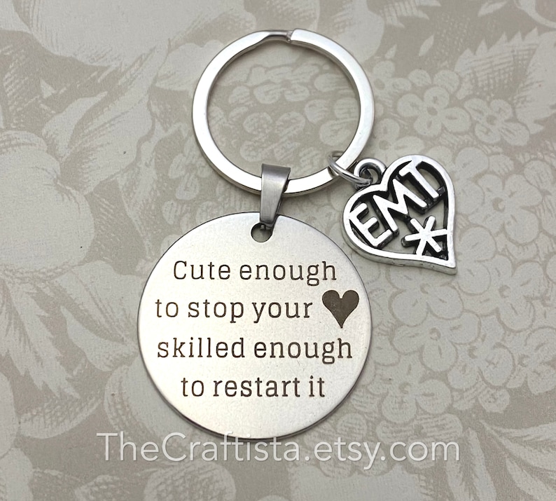 May include: Silver keychain with a round charm that reads "Cute enough to stop your heart, skilled enough to restart it."  A smaller heart charm with "EMT*" engraved on it hangs from the keychain.