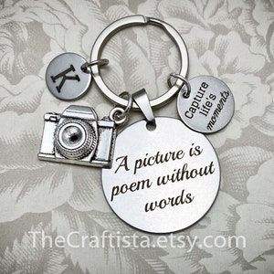 May include: Silver keychain with a camera charm, a round charm with the text "A picture is a poem without words", and a smaller charm with the text "Capture life's moments".