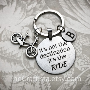 May include: Silver keychain with a bicycle charm and a round tag that reads "It's not the destination it's the RIDE". The keychain also has a small charm with the letter "B" on it.