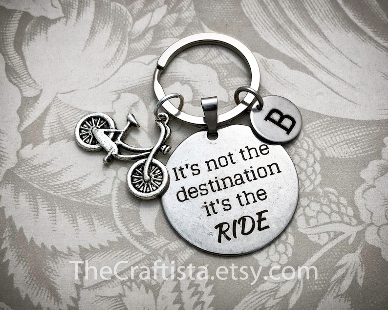 May include: Silver keychain with a bicycle charm and a round tag that reads "It's not the destination it's the RIDE". The keychain also has a small charm with the letter "B" on it.