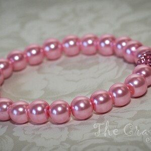 K&ouml;nnte beinhalten: Ein rosa Perlenarmband mit einem rosa Strass-Akzent.