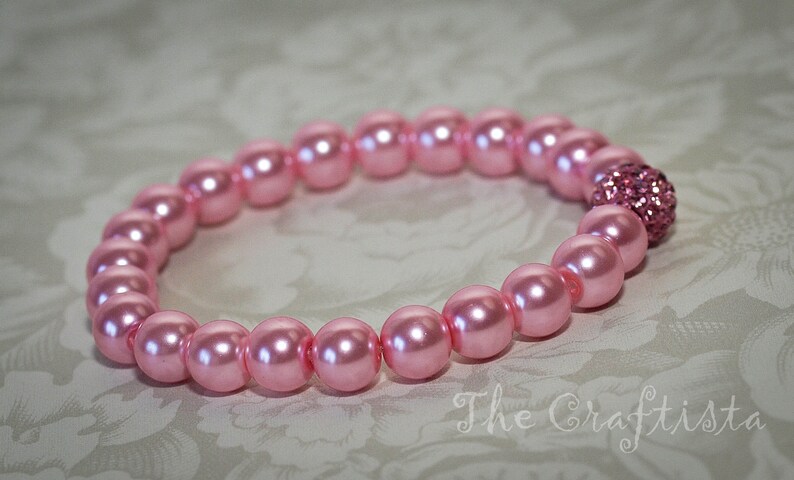 K&ouml;nnte beinhalten: Ein rosa Perlenarmband mit einem rosa Strass-Akzent.