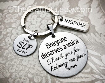 May include: Silver keychain with three charms. The largest charm is round and says "Everyone deserves a voice. Thank you for helping me find mine." The middle charm is round and says "This SLP rocks!" The smallest charm is rectangular and says "INSPIRE".