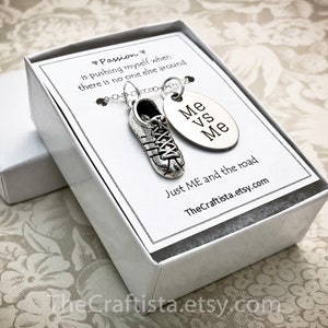 Puede incluir: Un collar de plata con un dije de zapato y un dije redondo que dice "Me vs Me". El collar está en una caja blanca con el texto "Passion is pushing myself when there is no one else around. Just ME and the road. TheCraftista.etsy.com"