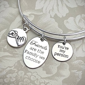 May include: Silver charm bracelet with three charms. The charms feature the text "Friends are the family we choose", "You're my person", and a design of two hands clasped together.
