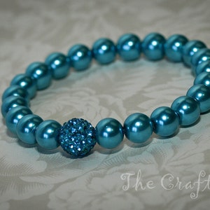 May include: A teal blue beaded bracelet with a sparkly blue rhinestone center.