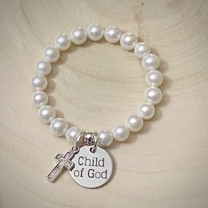 May include: White pearl bracelet with a silver charm that says "child of God" and a small silver cross.