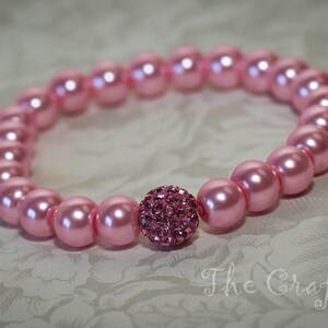K&ouml;nnte beinhalten: Ein rosa Perlenarmband mit einem rosafarbenen Strassstein in der Mitte.