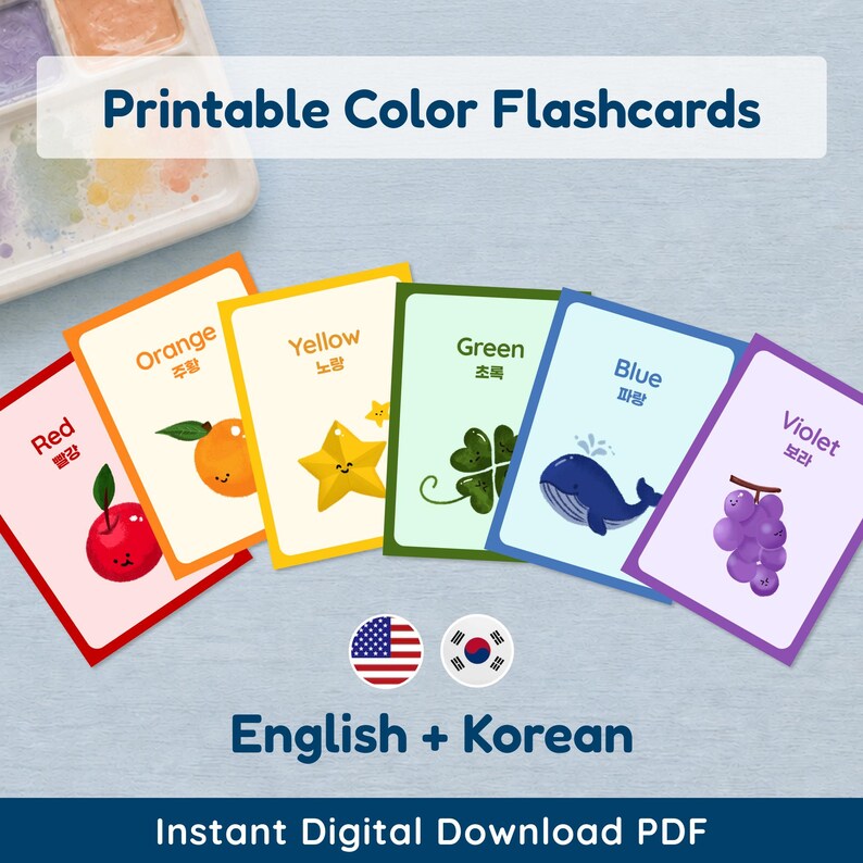 Six vibrant color flashcards are fanned out on a light blue surface, featuring colors from red to violet. Each card displays the color name in English and its Korean translation, along with a charming illustration: a red apple, an orange fruit, a yellow star, a green four-leaf clover, a blue whale, and purple grapes. A watercolor palette is visible in the background. Overlay text reads "Printable Color Flashcards," "English + Korean," and "Instant Digital Download PDF."