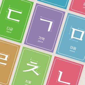 Close-up view of colorful Korean jamo flashcards showing Hangul consonants, stroke order arrows, Korean character names, and romanized pronunciation.