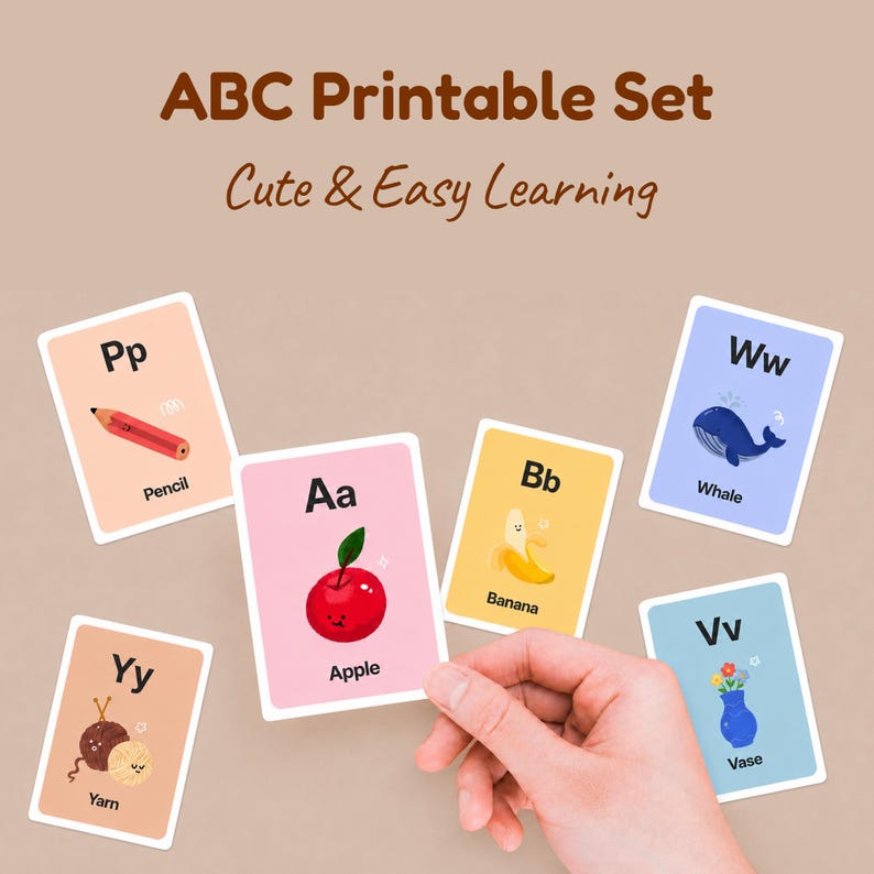 A person's hand holding a pink 'Aa for Apple' card among other scattered alphabet cards like Pencil, Whale, and Yarn. The title reads 'ABC Printable Set - Cute & Easy Learning' on a neutral background.