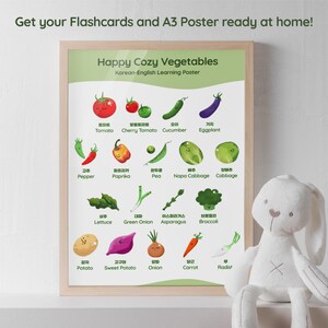 A framed poster titled "Happy Cozy Vegetables" with Korean-English text, featuring colorful illustrations of various vegetables like tomatoes, eggplant, and carrots. The text "Get your Flashcards and A3 Poster ready at home!" is at the top. A white stuffed bunny is in the foreground.