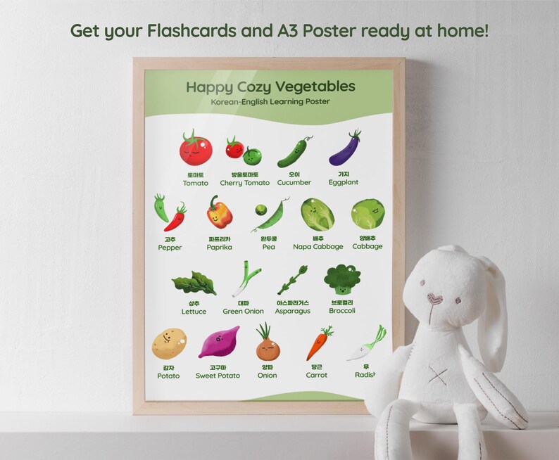 A framed poster titled "Happy Cozy Vegetables" with Korean-English text, featuring colorful illustrations of various vegetables like tomatoes, eggplant, and carrots. The text "Get your Flashcards and A3 Poster ready at home!" is at the top. A white stuffed bunny is in the foreground.