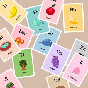 A top-down view of various hand-drawn alphabet cards scattered randomly, showcasing the consistent cozy art style and pastel color palette of the 'Happy Cozy Friends' brand.