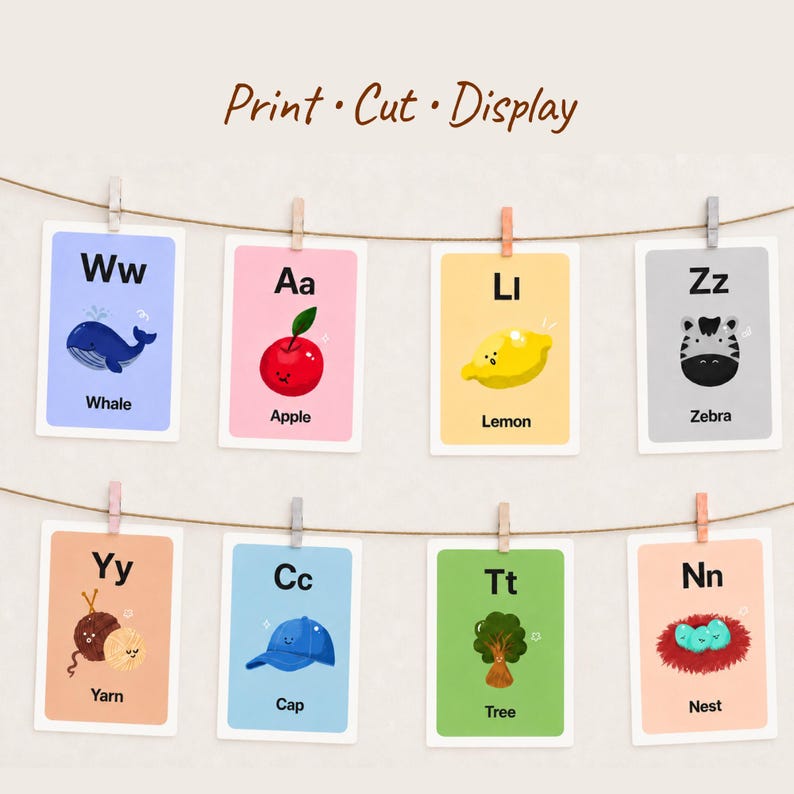 Eight colorful alphabet cards, including Whale, Apple, Lemon, and Zebra, are hung on a string with wooden clothespins against a plain wall. The title 'Print · Cut · Display' suggests home decor or classroom use.