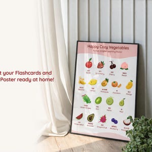 Lifestyle image of a Korean-English fruit learning poster displayed in a black frame on the floor beside a curtain, showing illustrated bilingual fruit names and text about printing flashcards and an A3 poster at home.
