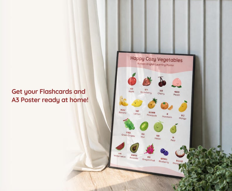 Lifestyle image of a Korean-English fruit learning poster displayed in a black frame on the floor beside a curtain, showing illustrated bilingual fruit names and text about printing flashcards and an A3 poster at home.