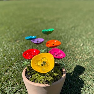 Puede incluir: Una maceta de terracota llena de musgo y arte de jardín colorido hecho a mano. El arte presenta piezas vibrantes en forma de flor, brillantes, en rojo, amarillo, rosa, naranja, morado, azul y verde, cada una con una cuenta de vidrio central.