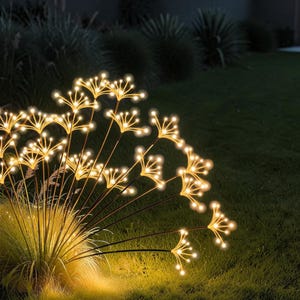 Può includere: Apparecchio di illuminazione decorativo per esterni con più steli e luci a LED bianco caldo. Le luci sono disposte a grappolo, simili a un dente di leone o a fuochi d'artificio. L'apparecchio è posizionato in un'area erbosa, creando un bagliore soffuso e invitante.