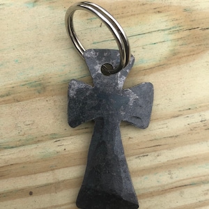 May include: A black metal cross keychain with a silver ring. The cross is made of hammered metal and has a rustic look.