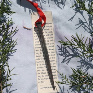 May include: A rusty nail with a red ribbon attached to it. The nail is hanging from a branch of a Christmas tree. The text on the tag reads: "The nail that hangs by the tree but for the Christ only He could for us, with no such as this. Hand forged by John."