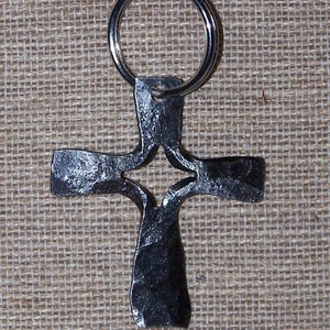 May include: A silver metal key chain with a black metal cross charm. The cross has a cut-out design in the center.
