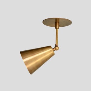 May include: A brass-colored, cone-shaped ceiling spotlight fixture. The fixture has a round base and a pivoting head, allowing for adjustable light direction. The design is minimalist and modern, suitable for various interior styles.
