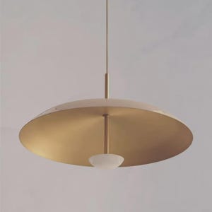 May include: A modern, gold-toned pendant light fixture. The light has a large, circular shade with a downward-facing, frosted glass bowl. The fixture is suspended from a thin rod.