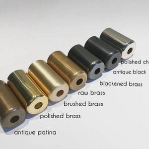 May include: A collection of cylindrical metal objects in various finishes, including antique patina, polished brass, and polished chrome. The image displays the names of each finish: antique patina, polished brass, brushed brass, raw brass, blackened brass, antique black, and polished chrome.