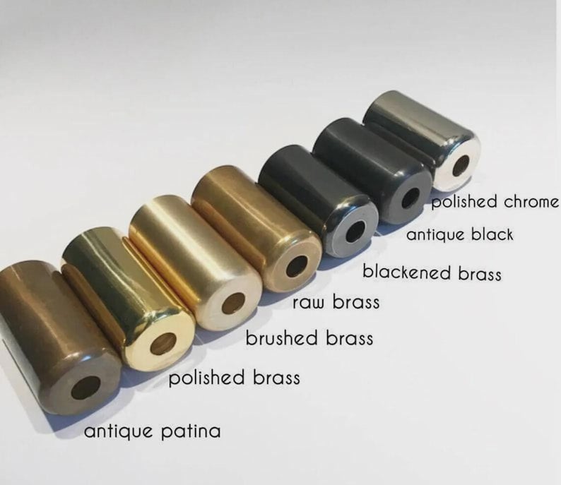 May include: A collection of cylindrical metal objects in various finishes, including antique patina, polished brass, and polished chrome. The image displays the names of each finish: antique patina, polished brass, brushed brass, raw brass, blackened brass, antique black, and polished chrome.