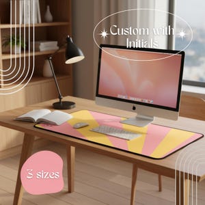 May include: A desk setup featuring a pink and yellow mousepad with a sunburst design. The mousepad is under a computer, keyboard, and mouse. The text "Custom with Initials" and "3 sizes" are also visible.