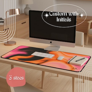 Puede incluir: Una configuración de escritorio con una computadora, teclado y mouse sobre una colorida alfombrilla de ratón. La alfombrilla tiene un diseño abstracto en negro, rosa y naranja. El texto en la alfombrilla dice "Custom with Initials" y "3 sizes". Un cuaderno y un bolígrafo también están en el escritorio.