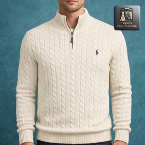 May include: A cream cable-knit sweater with a quarter-zip neckline and a navy blue embroidered logo. The sweater features a mock neck and long sleeves. The image also includes a Trendy Fashion Vibe logo.