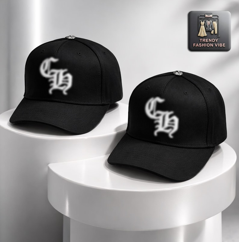 May include: Two black baseball caps with a curved brim are displayed. Each cap features a white, stylized letter design on the front. The caps are on a white surface. A small silver button is on top of each cap. The caps are part of the Trendy Fashion Vibe collection.