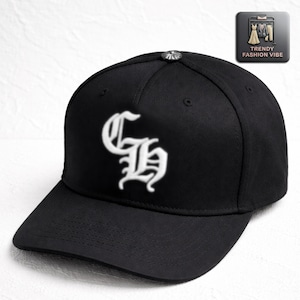 Puede incluir: Gorra de béisbol negra con visera curva y diseño bordado blanco en la parte delantera. La gorra tiene un botón plateado en la parte superior y un logotipo de Trendy Fashion Vibe.