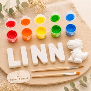 Può includere: Kit artigianale in legno con vasetti di vernice rossa, arancione, gialla, verde e blu. Include lettere di legno bianche che compongono "LINN", una statuina di dinosauro bianca e due pennelli. Ideale per progetti creativi.