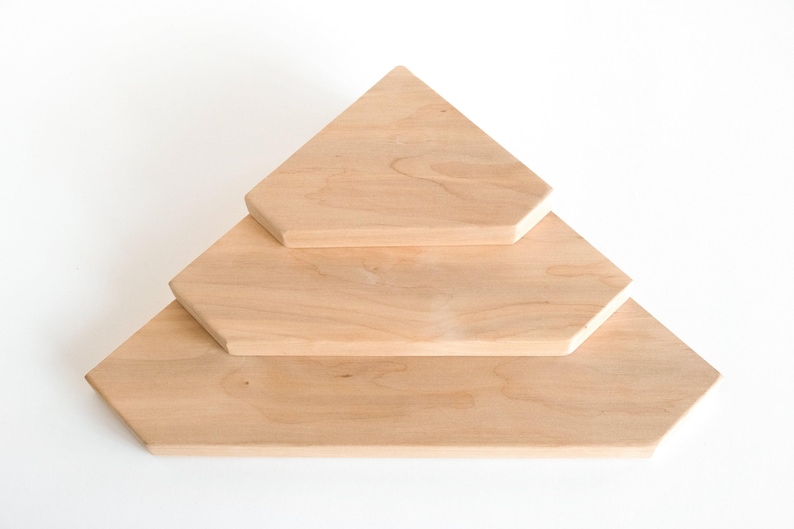 Puede incluir: Tres estantes de madera sin terminar dispuestos en forma escalonada. Los estantes son de color claro, con una veta de madera natural. El estante superior es triangular, el del medio es un hex&aacute;gono y el inferior es un hex&aacute;gono m&aacute;s grande.