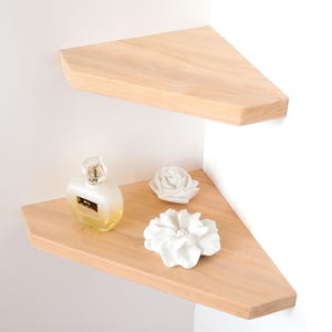 Puede incluir: Dos estanter&iacute;as de esquina de madera clara montadas en una pared blanca. La estanter&iacute;a inferior contiene un frasco de perfume y dos flores decorativas de cer&aacute;mica blanca. Las estanter&iacute;as tienen forma triangular.