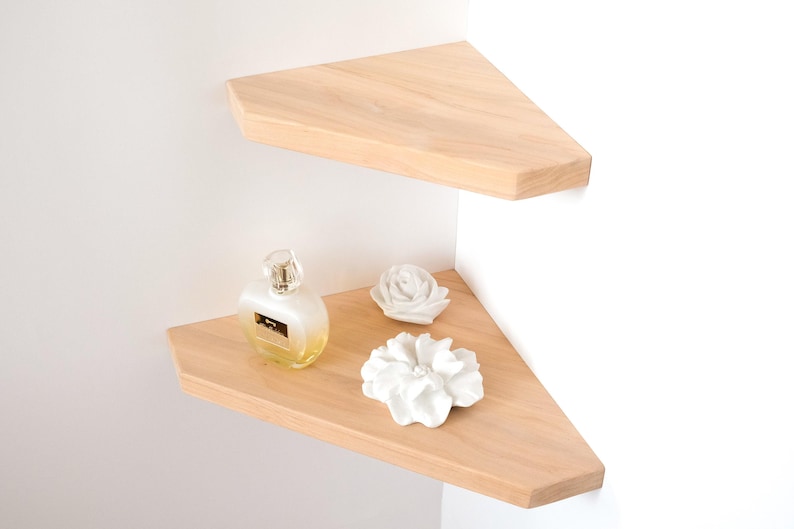 Puede incluir: Dos estanter&iacute;as de esquina de madera clara montadas en una pared blanca. La estanter&iacute;a inferior contiene un frasco de perfume y dos flores decorativas de cer&aacute;mica blanca. Las estanter&iacute;as tienen forma triangular.