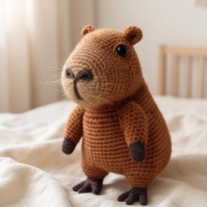 Peut inclure: Une peluche capybara crochetée marron avec un corps arrondi, de petites oreilles et des pattes marron foncé. La figurine présente des yeux en plastique noir, un nez brodé et de fines moustaches claires partant de la zone du museau en laine.